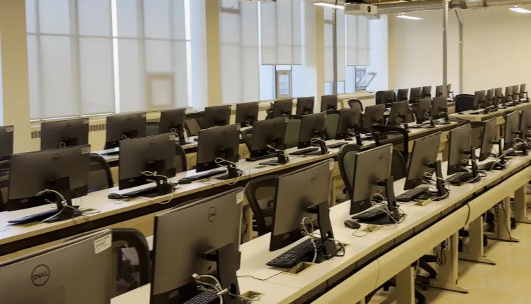 Rows of computer setups, showing the back side of the monitors.